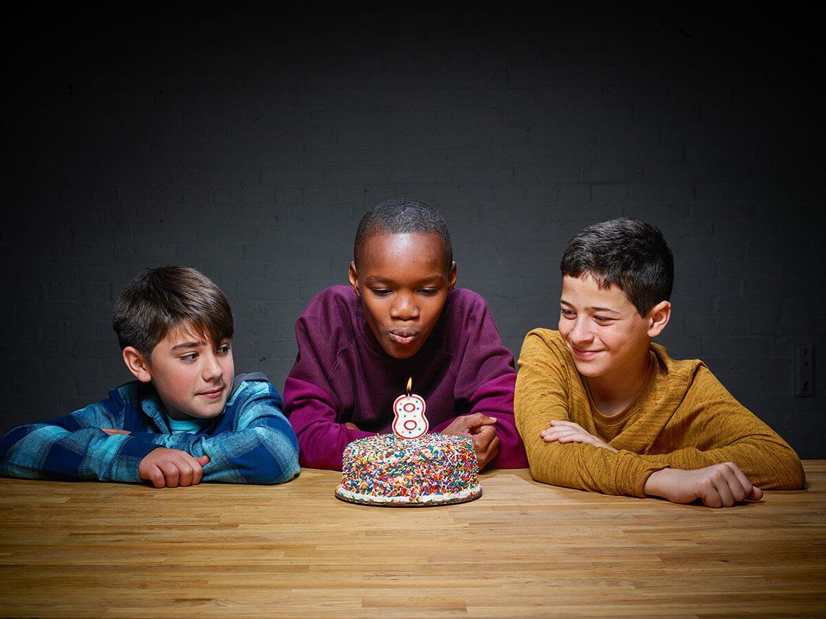 Boy blows candle on birthday cake with his 2 friends.