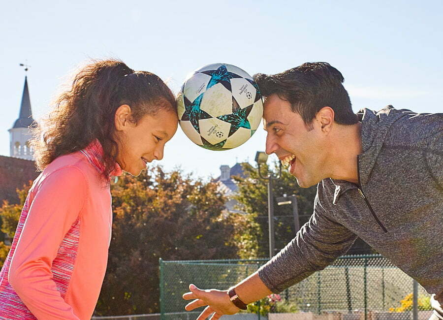 Dad and daughter holding a soccer ball together with their heads.